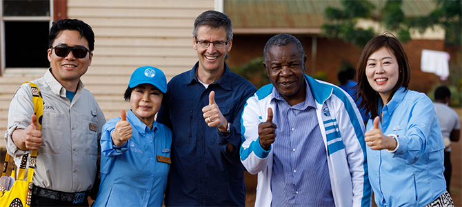 670x300_Day1_08_NuSkin Nu Skin Founder Steve Lund, Napoleon Dzombe, and Nu Skin sales leaders and employees pose for a picture by giving a thumbs up.
